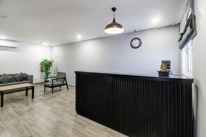 Un área de recepción con mostrador negro, un reloj, un sofá, una silla y una planta colgante.