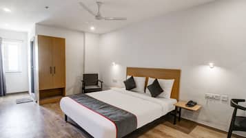 A hotel room with a bed, a chair, a desk, a wardrobe, and a ceiling fan.
