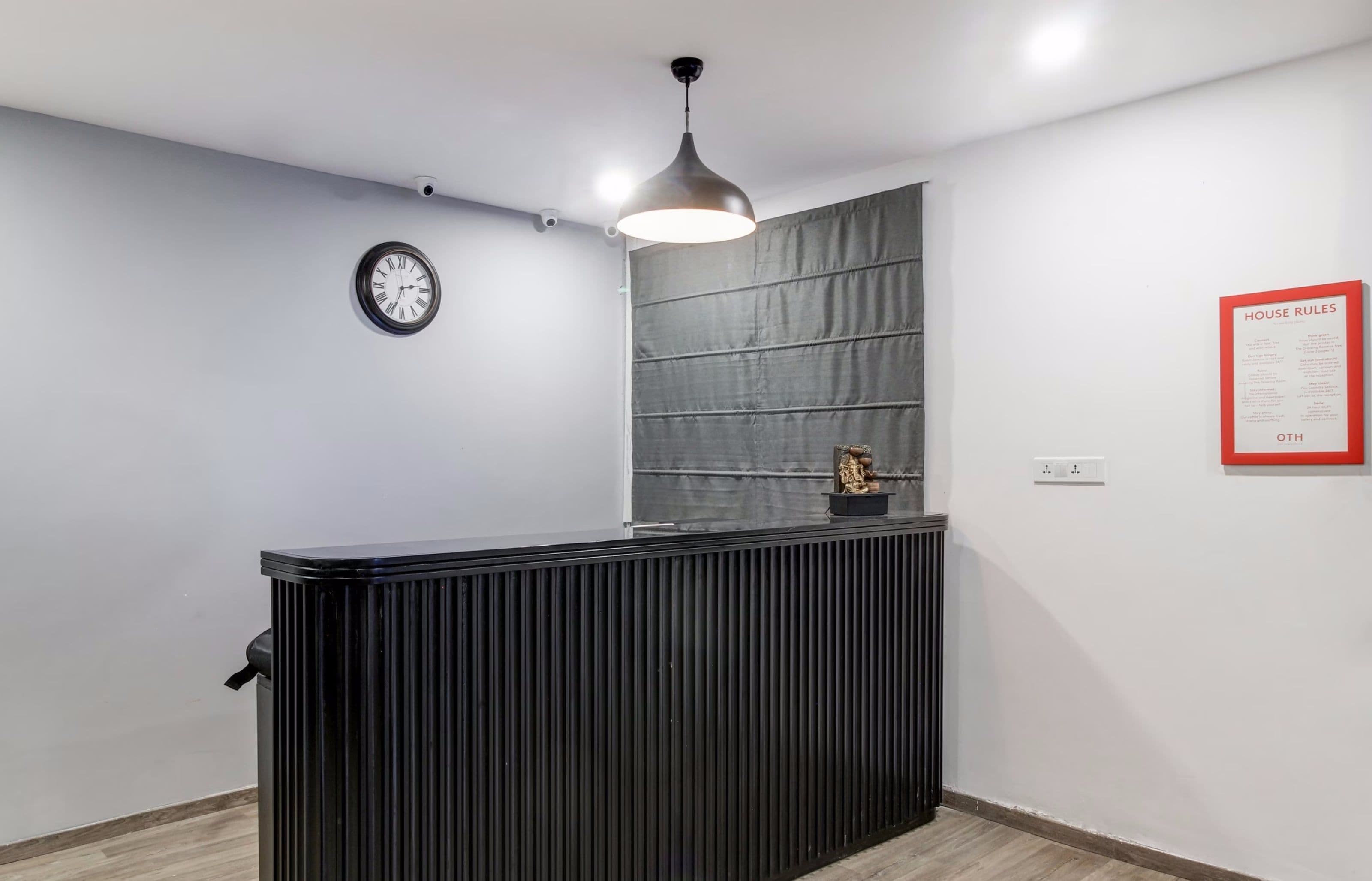 A reception desk with a clock, a wall-mounted light fixture, and a framed notice board.