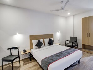Una habitación de hotel con cama, mesitas de noche, una silla, armario y ventilador de techo.