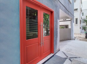 Una puerta roja con un panel de vidrio, una pared de concreto y una zona pavimentada con una motocicleta.