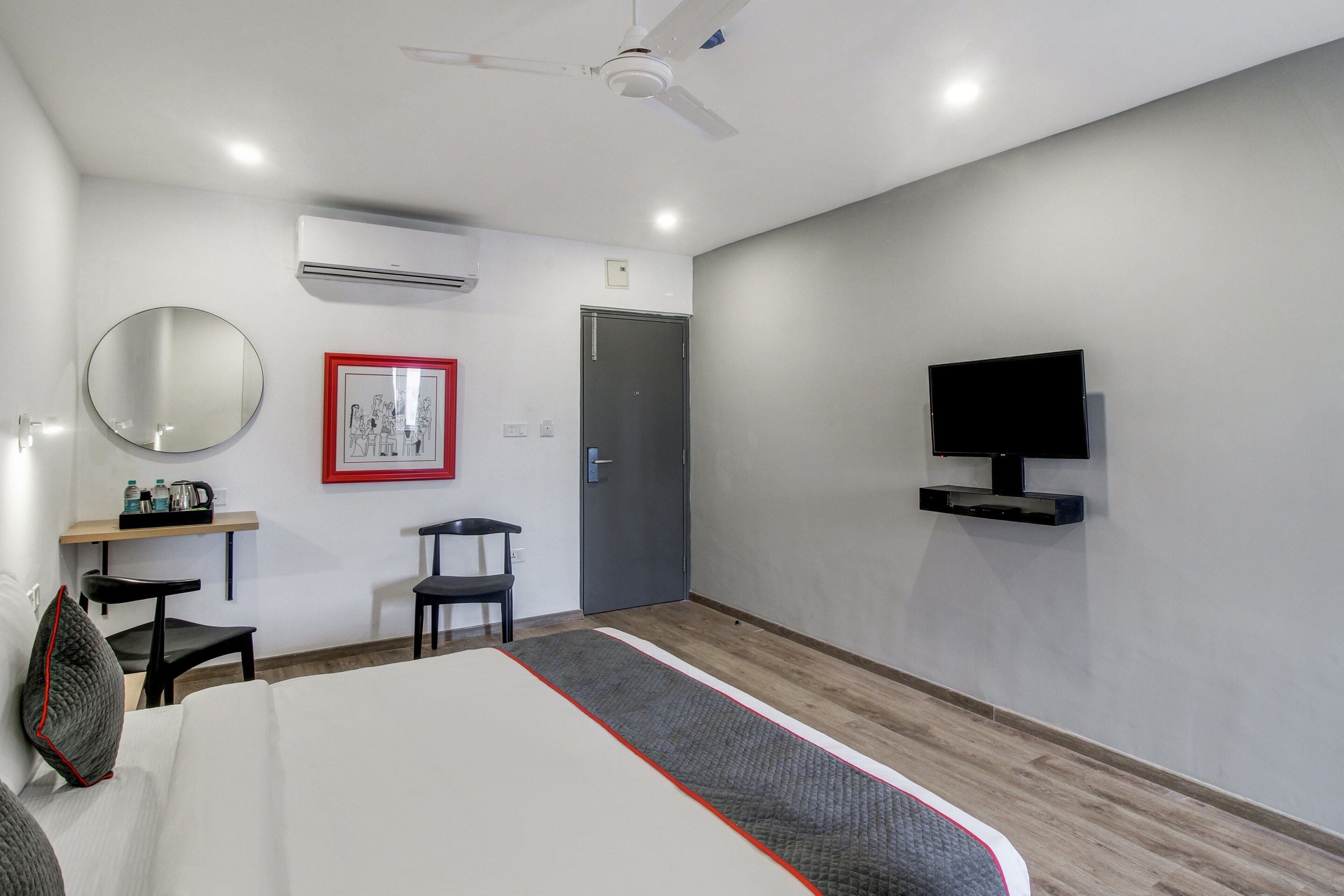 A hotel room with a bed, a desk with a chair, a television mounted on the wall, and a door.