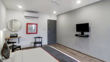 A hotel room with a bed, a desk with a chair, a television mounted on the wall, and a door.