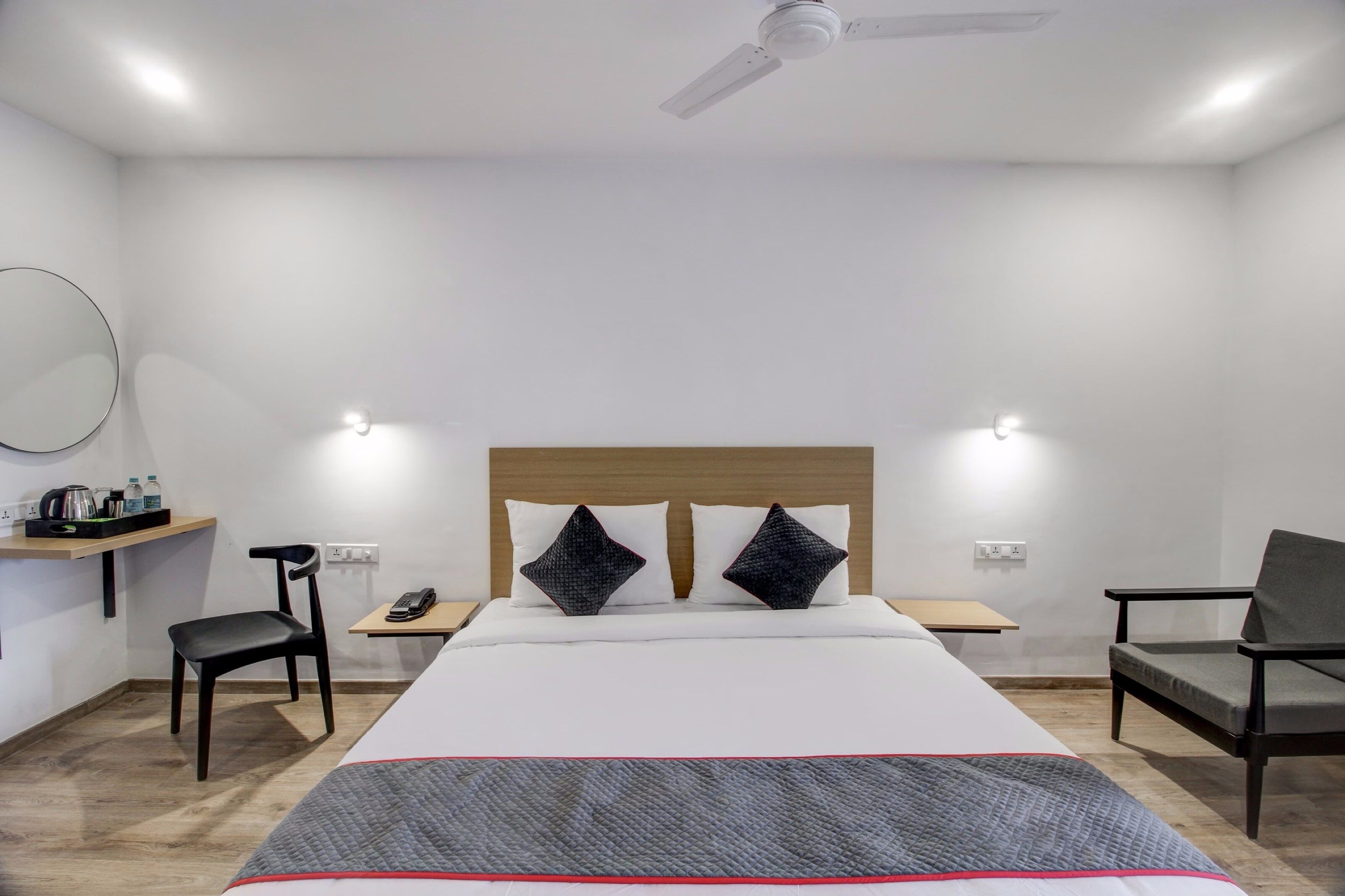 A hotel room with a bed, bedside tables, a chair, a desk, a mirror, and a ceiling fan.