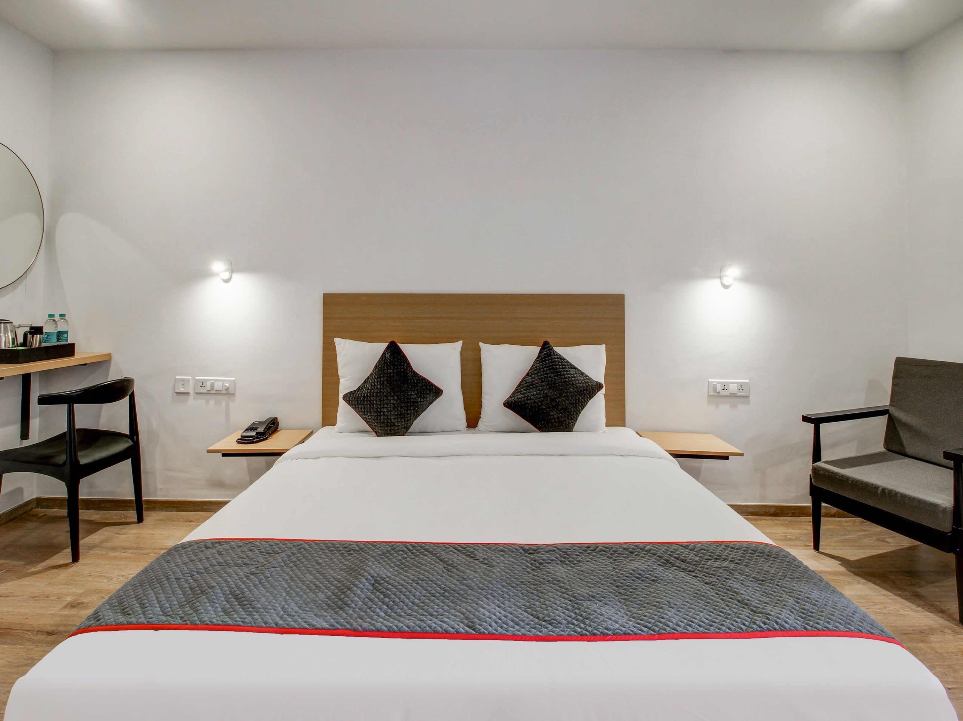 Ein Hotelzimmer mit einem Bett, zwei Nachttischen, einem Sessel, einem Schreibtisch und einem Spiegel.