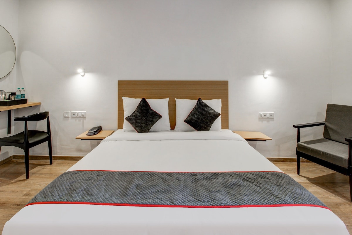 Quarto de hotel com cama, duas mesas de cabeceira, uma cadeira, escrivaninha e espelho.