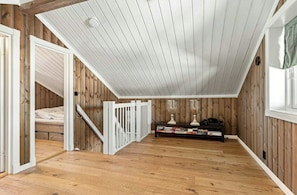 A loft bedroom with a sloped ceiling, wooden walls, a white railing, a bed, and a small table with books and decorative items.