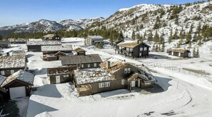 Ein schneebedecktes Dorf mit Holzhäusern, einem klaren Himmel und Bergen im Hintergrund.