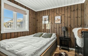 Ein Schlafzimmer mit einem Bett, einem Fenster, Holzwänden und gerahmten Bildern.