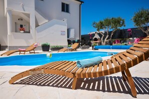 Uma área à beira da piscina com espreguiçadeiras de madeira, uma toalha azul e uma piscina de águas cristalinas.