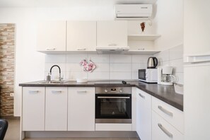 A modern kitchen with white cabinetry, a built-in oven, a microwave, and a coffee maker. - Villa Feliks ZadarVillas (Ljubac)