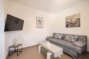 Un salon comprenant un canapé, une table basse, un téléviseur fixé au mur et deux œuvres d’art encadrées.
