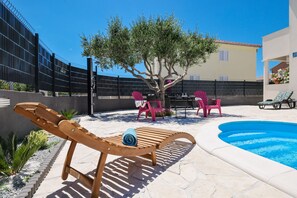 A poolside area with a wooden lounge chair, a small table, and pink chairs. - Villa Feliks ZadarVillas (Ljubac)