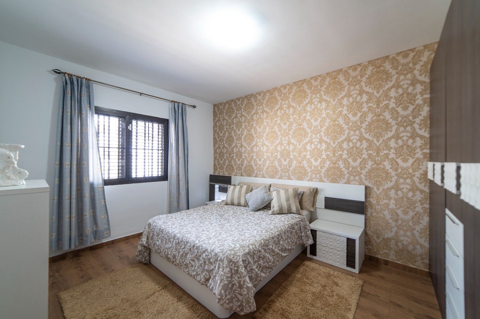 A bedroom with a bed, curtains, a patterned wall, and a window.