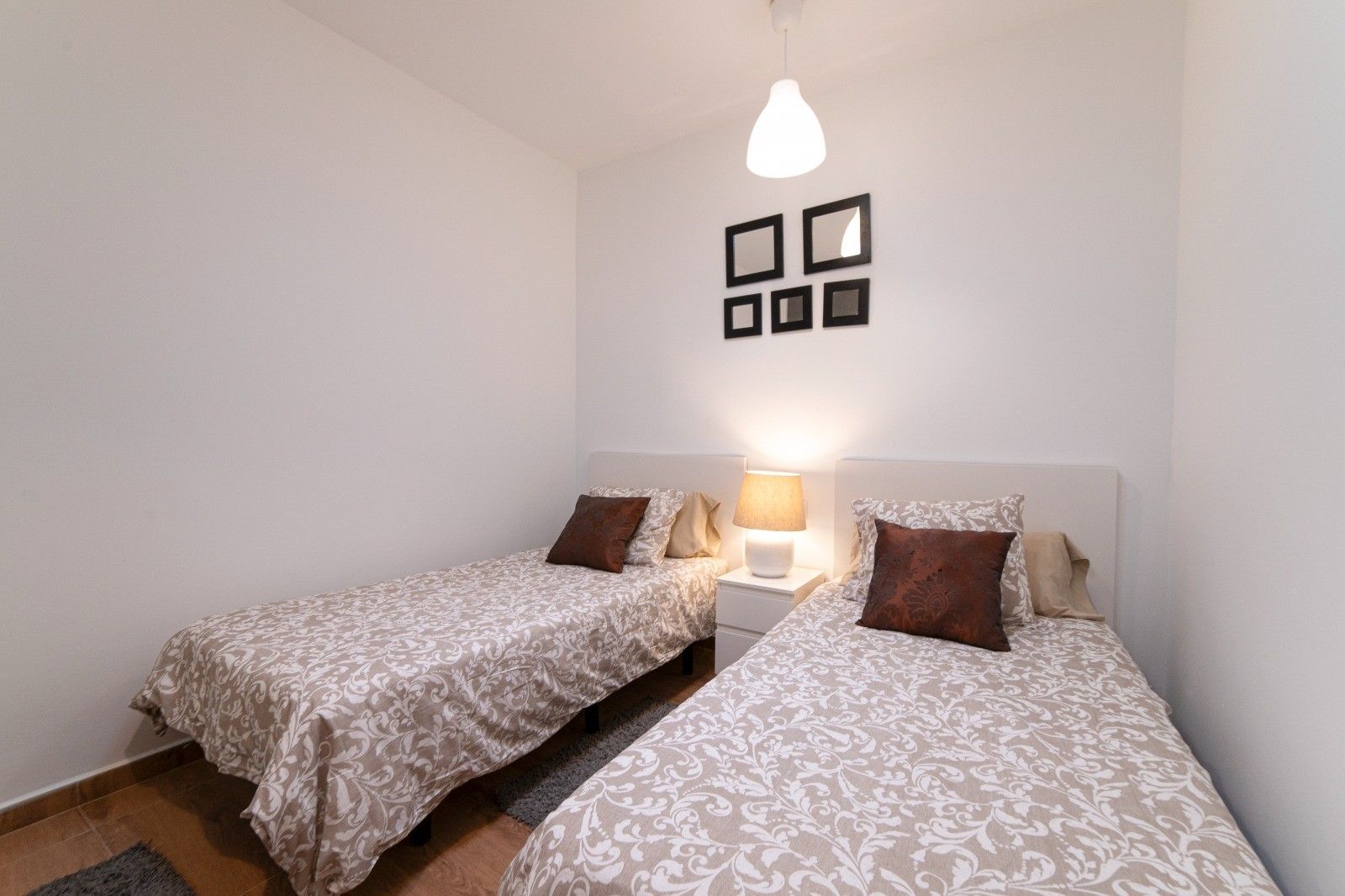 Un dormitorio con dos camas individuales, una mesita de noche con lámpara y una lámpara de pared.