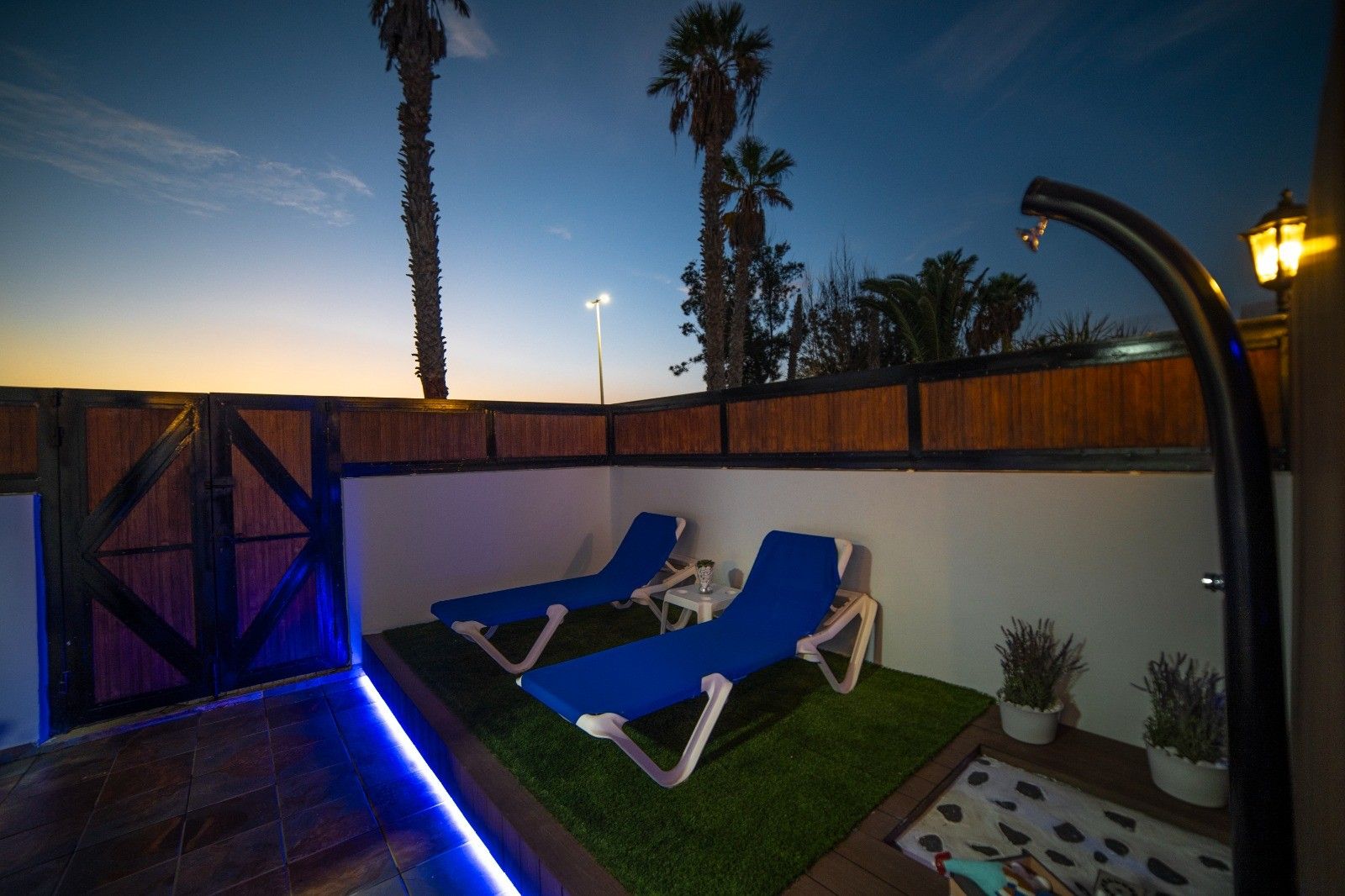 An outdoor patio with two blue lounge chairs, a small table, and a decorative fence.
