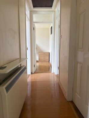 Un pasillo estrecho con suelo de madera que lleva a una habitación con cama y puerta.