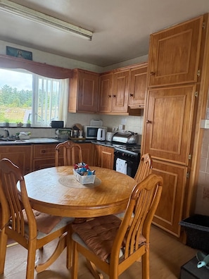 Una cocina con armarios de madera, una mesa redonda con sillas, un microondas, un tostador y una ventana con vistas a la vegetación.
