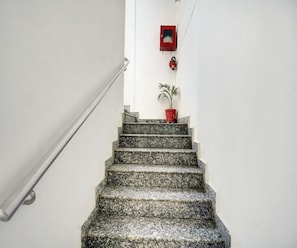 Eine Treppe mit Granitstufen, die nach oben führt, ein roter Feuerwarnschalter an der Wand und eine Topfpflanze oben.