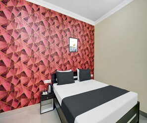 Ein Hotelzimmer mit Wand im geometrischen Muster, einem Bett mit schwarz-weißer Bettwäsche, einem Nachttisch mit Lampe und einem gerahmten Bild an der Wand.