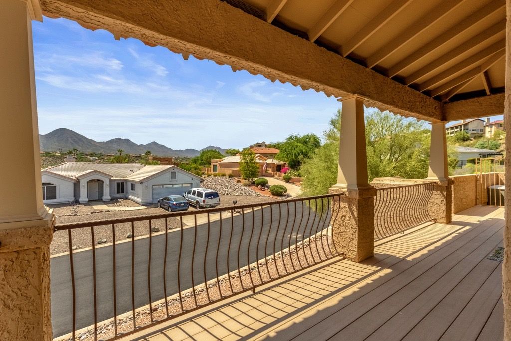 Un balcón techado con vistas a una zona residencial, que incluye casas y una calle.