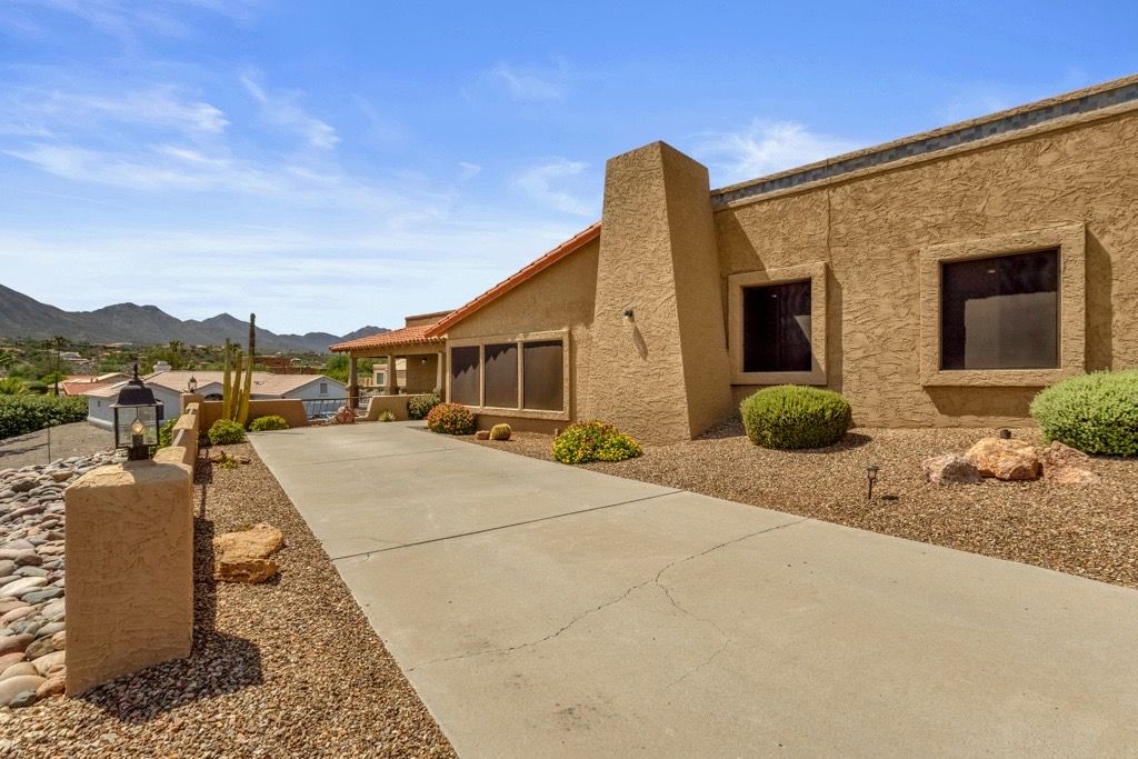A residential building with a concrete driveway, stone landscaping, and a mountain backdrop.
