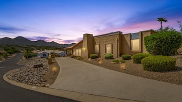 A residential area with a modern house featuring a driveway, landscaped garden, and a mountain backdrop.