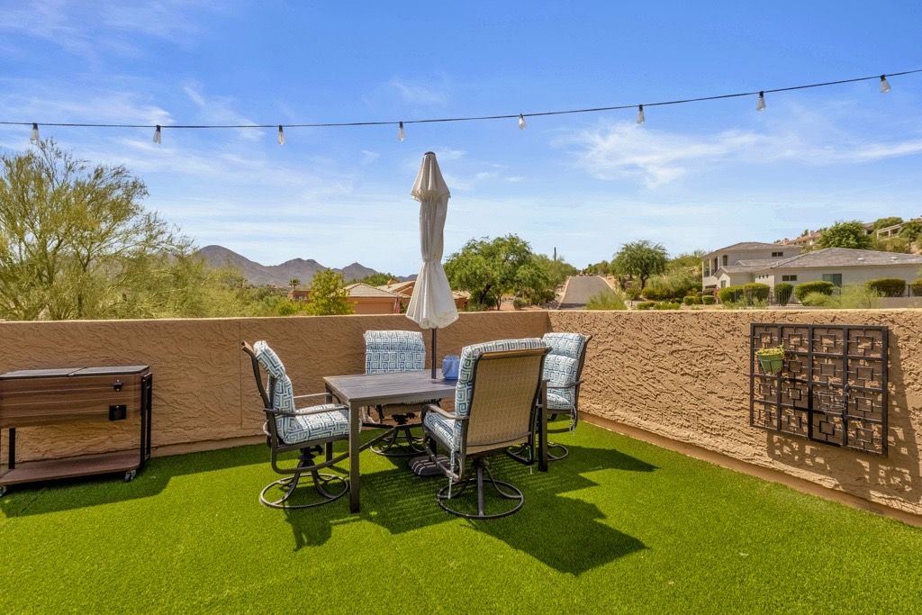 An outdoor patio with a table and chairs, a grill, and string lights.
