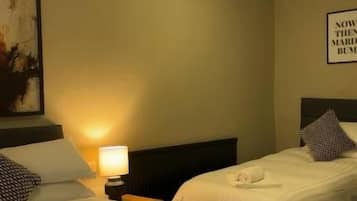 Habitación de hotel con dos camas, una mesita de noche con lámpara y una cita enmarcada en la pared.