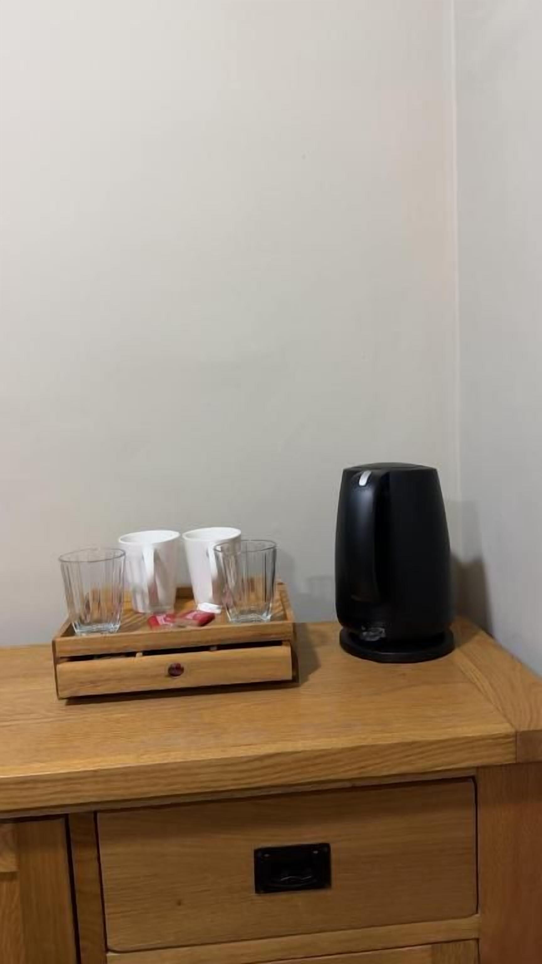 Una mesita de noche de madera con una cafetera negra y tres vasos en una bandeja.
