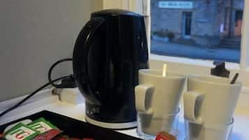 Una cafetera negra, dos tazas y una caja de bolsitas de té sobre una mesa junto a una ventana.
