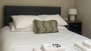A neatly made bed with white linens and a green patterned pillow, a bedside lamp, and a painting on the wall.