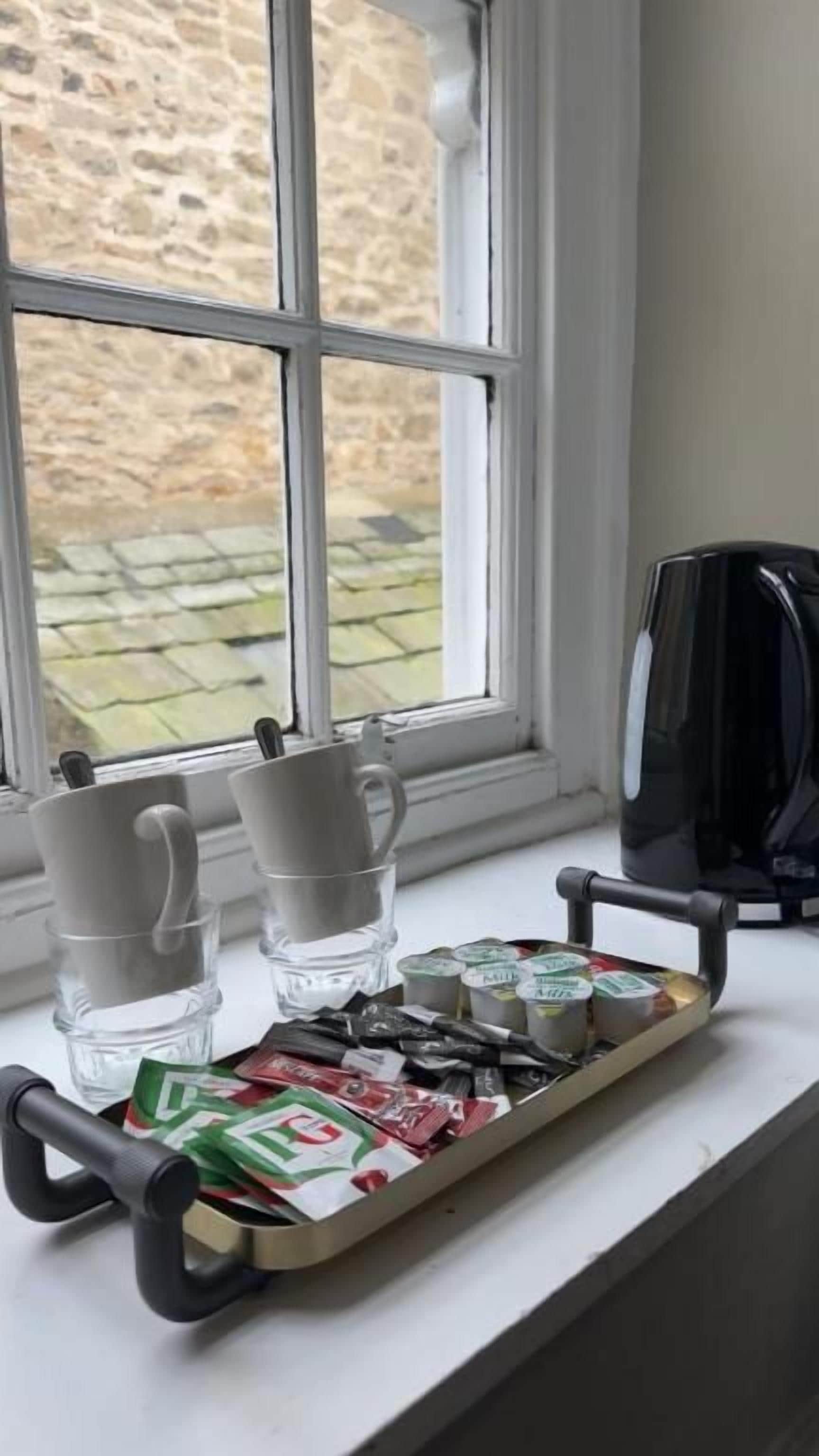 A tray with coffee cups and tea packets on a windowsill.