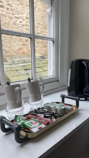 A tray with coffee cups and tea packets on a windowsill.
