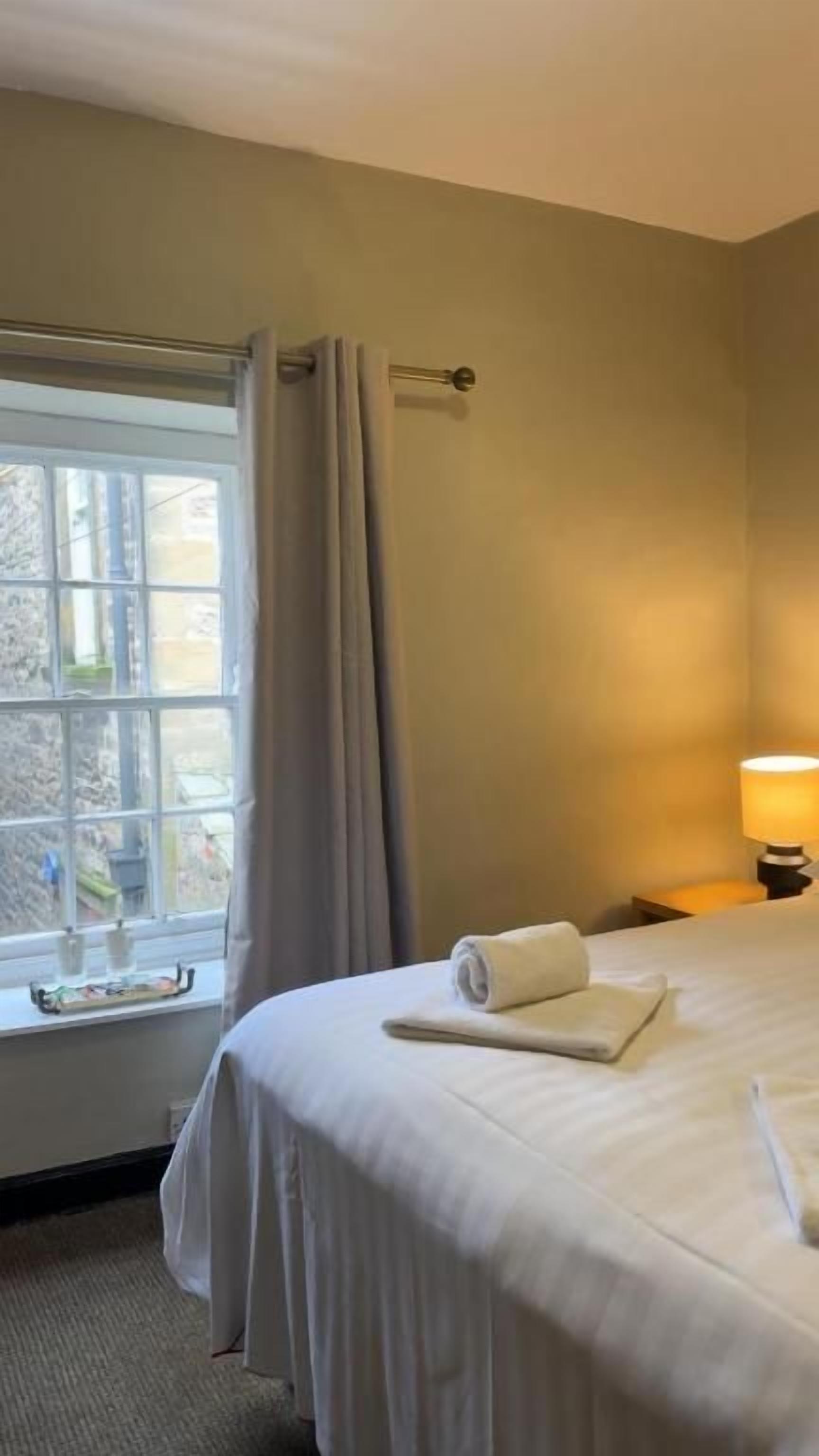 Una camera d'albergo con un letto, una finestra con tende, una lampada e vista sull'esterno.