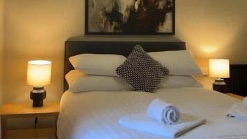 Een hotelkamer met een bed, twee nachtkastjes met lampen, een schilderij aan de muur en een opgemaakt bed met een handdoek.