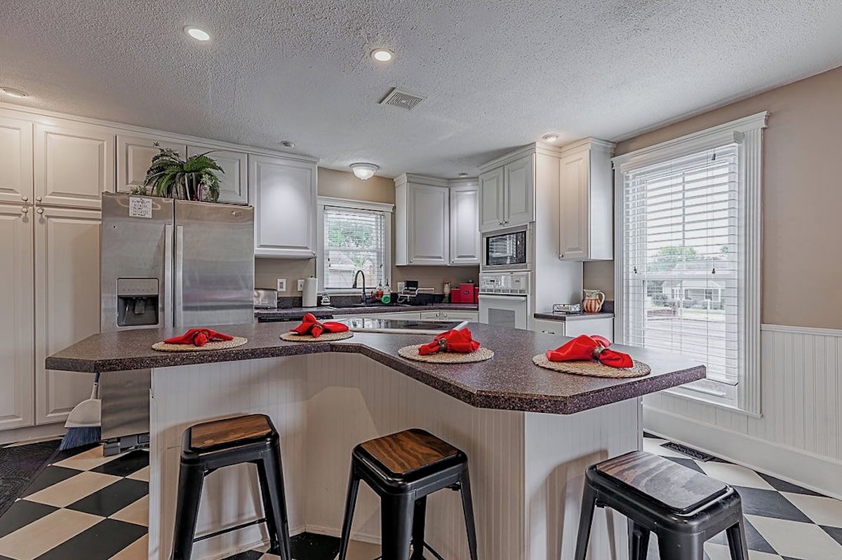 Una cocina moderna con muebles blancos, una isla central con taburetes y un suelo de cuadros.