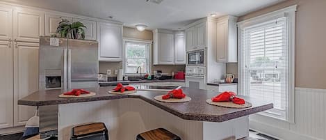 A modern kitchen with white cabinetry, a central island with stools, and a checkered floor.