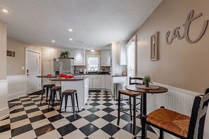 A kitchen with white cabinets, a black and white checkered floor, and a dining area with stools. - Historic 1851 Downtown Elizabethtown Home (Elizabethtown)