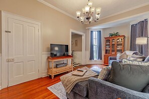 A living room with a television on a wooden stand, a sofa, a cabinet with glass doors, and a chandelier. - Historic 1851 Downtown Elizabethtown Home (Elizabethtown)