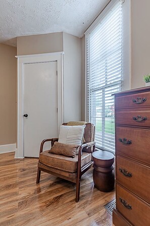 A room with a wooden floor, a chair with cushions, a wooden dresser with drawers, a door, and a window with blinds. - Historic 1851 Downtown Elizabethtown Home (Elizabethtown)