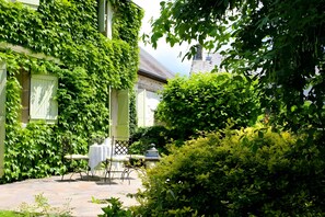A courtyard with a table and chairs, surrounded by lush greenery and a building with a green door. - Guest Room 'Chambre À L'étage' with Lake View and Wi-Fi (Chamborand)