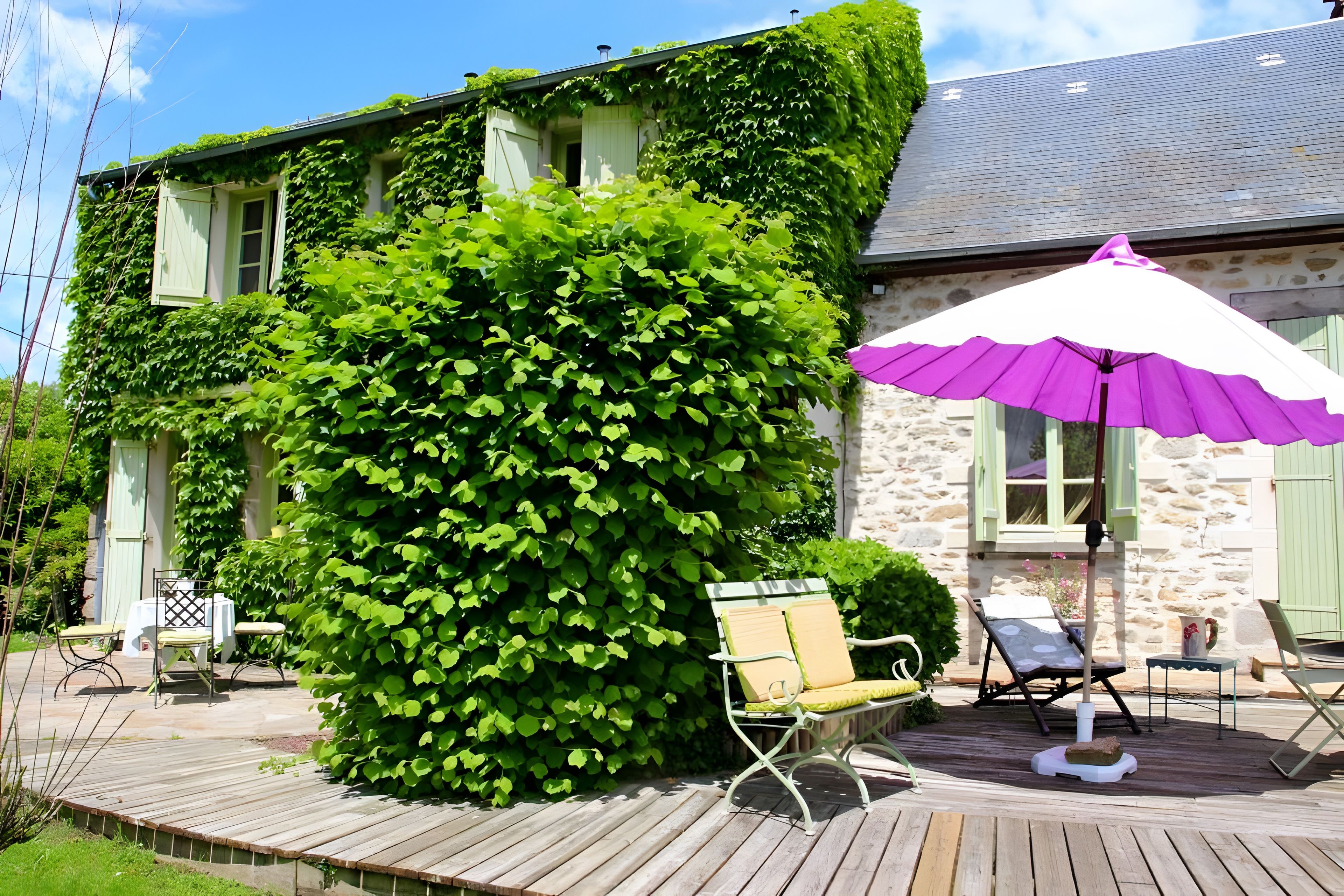 Ein Haus mit Efeu bewachsenen Wänden, einer Holzterrasse und Sitzgelegenheiten im Freien.