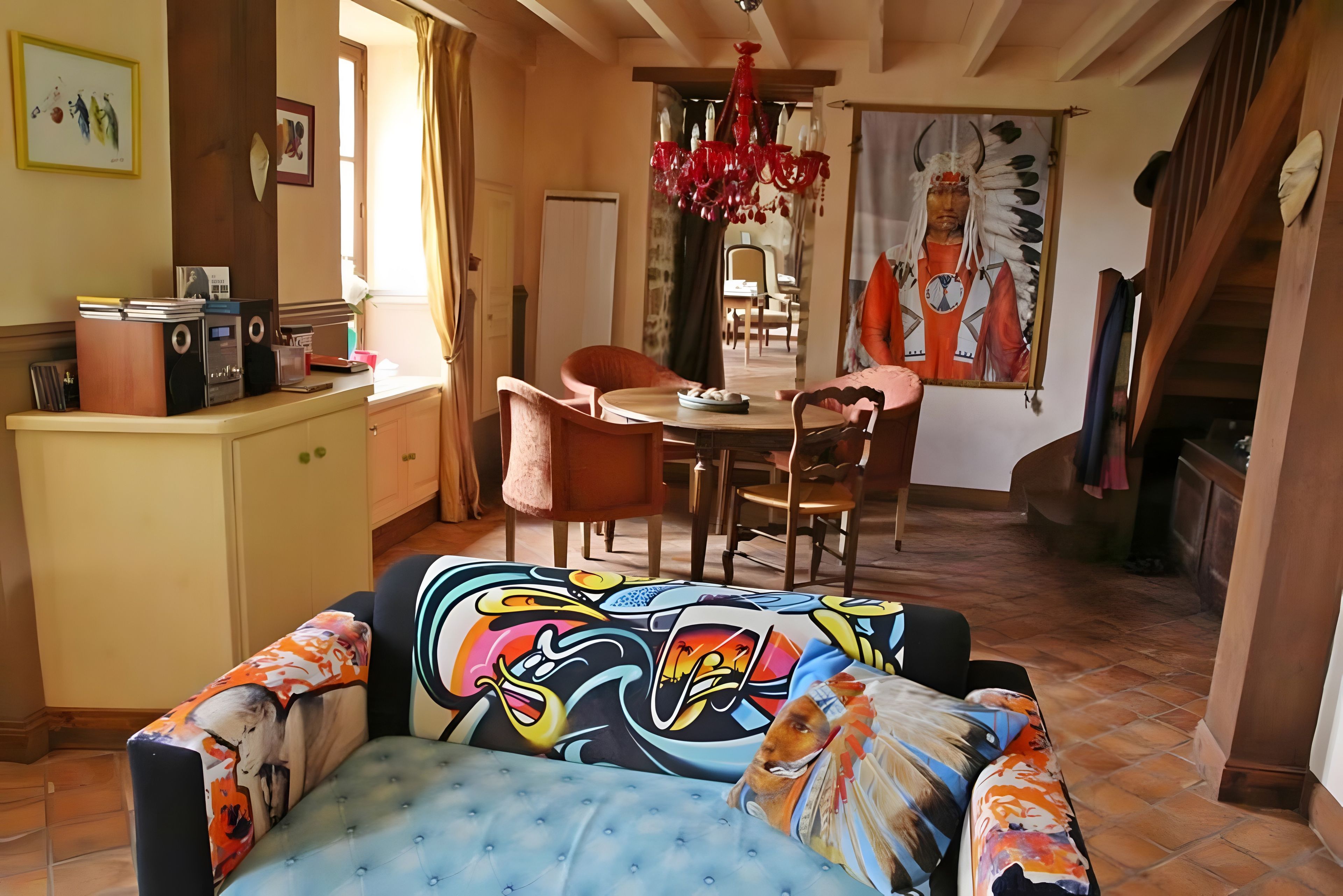 A dining area with a table and chairs, a kitchen area with a counter and appliances, and a colorful sofa with a unique design.
