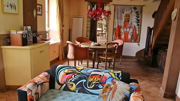 A dining area with a table and chairs, a kitchen area with a counter and appliances, and a colorful sofa with a unique design.