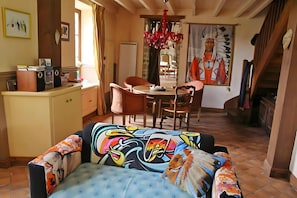 A dining area with a table and chairs, a kitchen area with a counter and appliances, and a colorful sofa with a unique design.