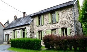 A stone building with green shutters, a visible chimney, and a small garden area. - Guest Room 'Chez Claire - Suite Vue Jardin' with Wi-Fi (Chamborand)