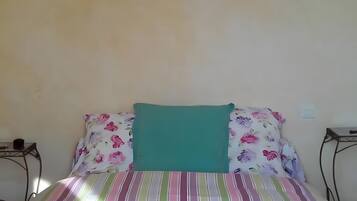 Ein Bett mit blumigem Bettzeug, einem türkisblauen Kissen und einem gerahmten Bild an der Wand.