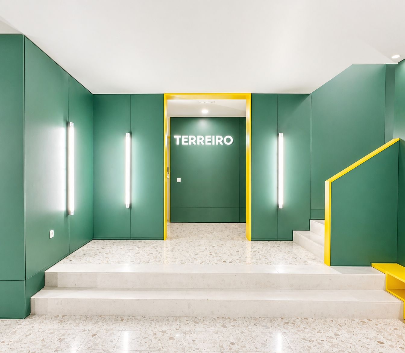 A modern interior with a terrazzo floor, green walls, and a staircase with yellow accents.