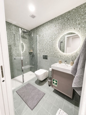 Un baño moderno con ducha envuelta en vidrio, inodoro y lavabo con toallero.